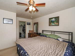 Bedroom with a textured ceiling, a walk in closet, light carpet, and ceiling fan