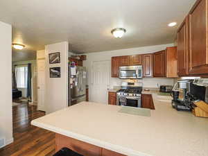 Kitchen featuring stainless steel appliances, a peninsula, light countertops, dark wood-style floors, and a textured ceiling