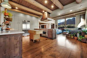 Kitchen featuring premium appliances, dark wood-style floors, island exhaust hood, open floor plan, and a wooden ceiling with exposed beams