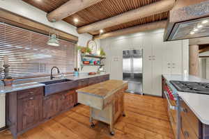 Dual tone kitchen with high end appliances, pendant lighting, light wood finished floors, light stone countertops, and a wooden ceiling with exposed beams