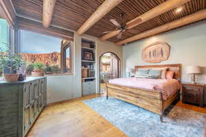 Bedroom featuring light wood-style flooring, a mountain view, a ceiling fan, a wooden ceiling with exposed beams, and arched walkways