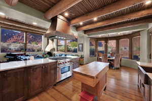 Kitchen with island exhaust hood, designer stove, light wood finished floors, a wood ceiling with exposed beams, and dark wood finish cabinetry
