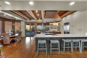 Dual tone kitchen with a breakfast bar area, a peninsula, a wooden ceiling with exposed beams, stainless steel appliances, and light wood finished floors