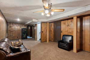 Living area with a textured ceiling, wooden walls, carpet floors, and a ceiling fan