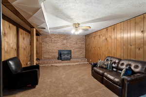 Living room with wood walls, carpet, a textured ceiling, ceiling fan, and a wood stove