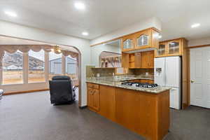 Kitchen featuring light stone countertops, white refrigerator with ice dispenser, dark colored carpet, tasteful backsplash, and a peninsula