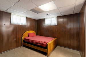 Bedroom featuring light carpet, wooden walls, and a drop ceiling