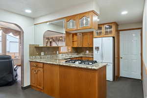 Kitchen with dark carpet, backsplash, light stone counters, and recessed lighting
