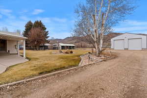 View of yard featuring an outbuilding, a detached garage, a patio area, a mountain view, and dirt driveway