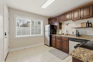 Kitchen with stainless steel appliances, open shelves, light stone counters, light tile patterned flooring, and dark wood finish cabinetry