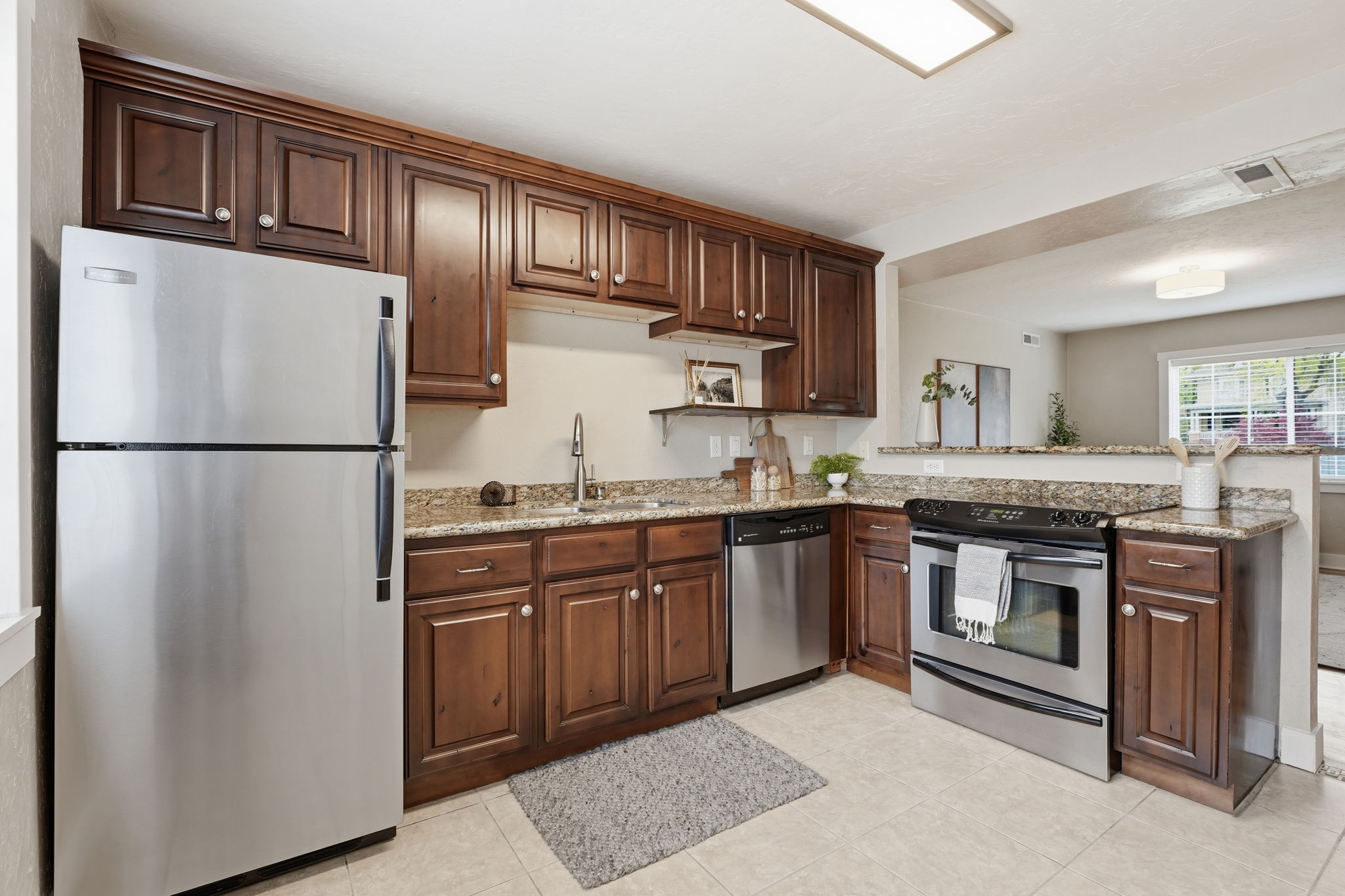 Kitchen with stainless steel appliances, light stone counters, dark wood finish cabinetry, and a peninsula