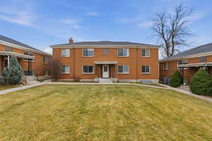 View of front facade with a chimney, a front yard, and brick siding