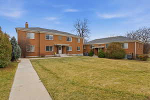 Back of house featuring a chimney, brick siding, and a lawn