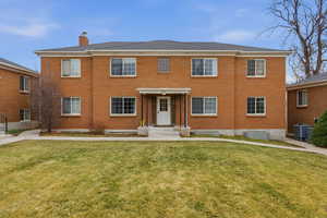Colonial house featuring brick siding, a chimney, and a front lawn