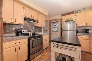 Kitchen with stainless steel appliances, backsplash, tile counters, and cream cabinets