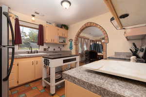 Kitchen with freestanding refrigerator, cream cabinetry, decorative backsplash, arched walkways, and stove