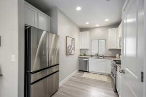 Kitchen featuring stainless steel appliances, white cabinets, light wood-style floors, recessed lighting, and light stone countertops