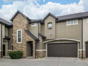 View of front facade featuring stucco siding, driveway, stone siding, and a garage