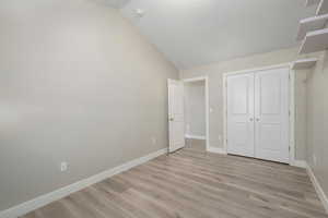 Unfurnished bedroom featuring light wood-style floors, lofted ceiling, and a closet