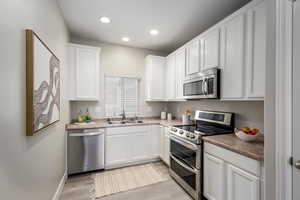 Kitchen with stainless steel appliances, white cabinets, light wood-style flooring, and recessed lighting