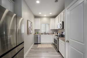 Kitchen featuring stainless steel appliances, white cabinetry, light wood finished floors, recessed lighting, and light stone countertops