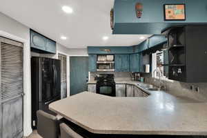 Kitchen with a peninsula, electric range, freestanding refrigerator, open shelves, and stainless steel microwave