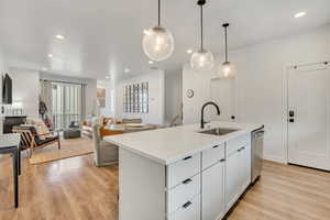 Kitchen with white cabinets, light wood-style flooring, a kitchen island with sink, open floor plan, and decorative light fixtures
