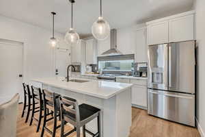 Kitchen featuring stainless steel appliances, light wood-style floors, white cabinets, decorative light fixtures, and a kitchen island with sink