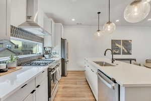 Kitchen featuring stainless steel appliances, white cabinetry, light wood-style flooring, pendant lighting, and a center island with sink