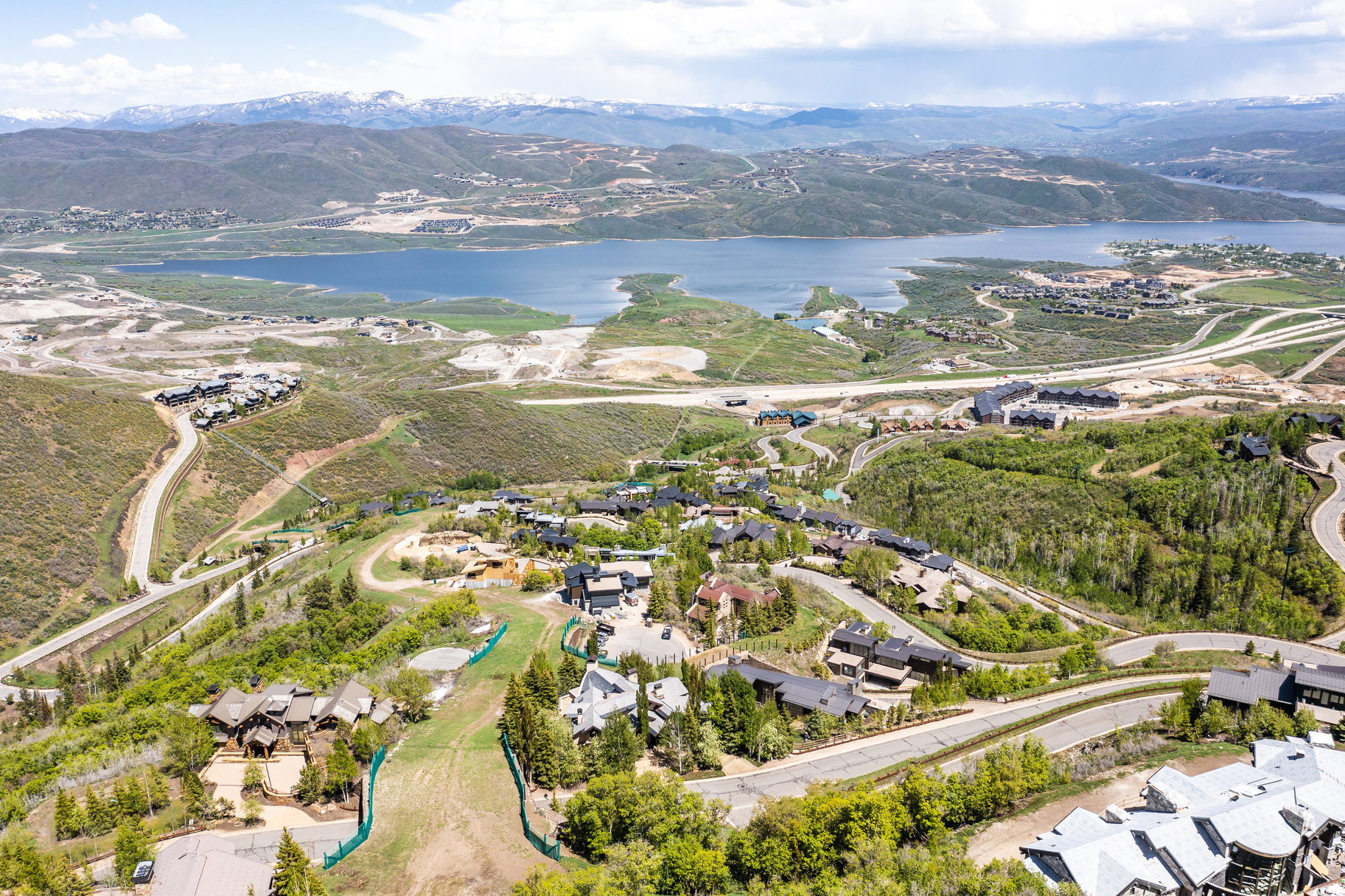 Expansive aerial showcasing a mountainous landscape with a large body of water, green hillsides, and a winding road system