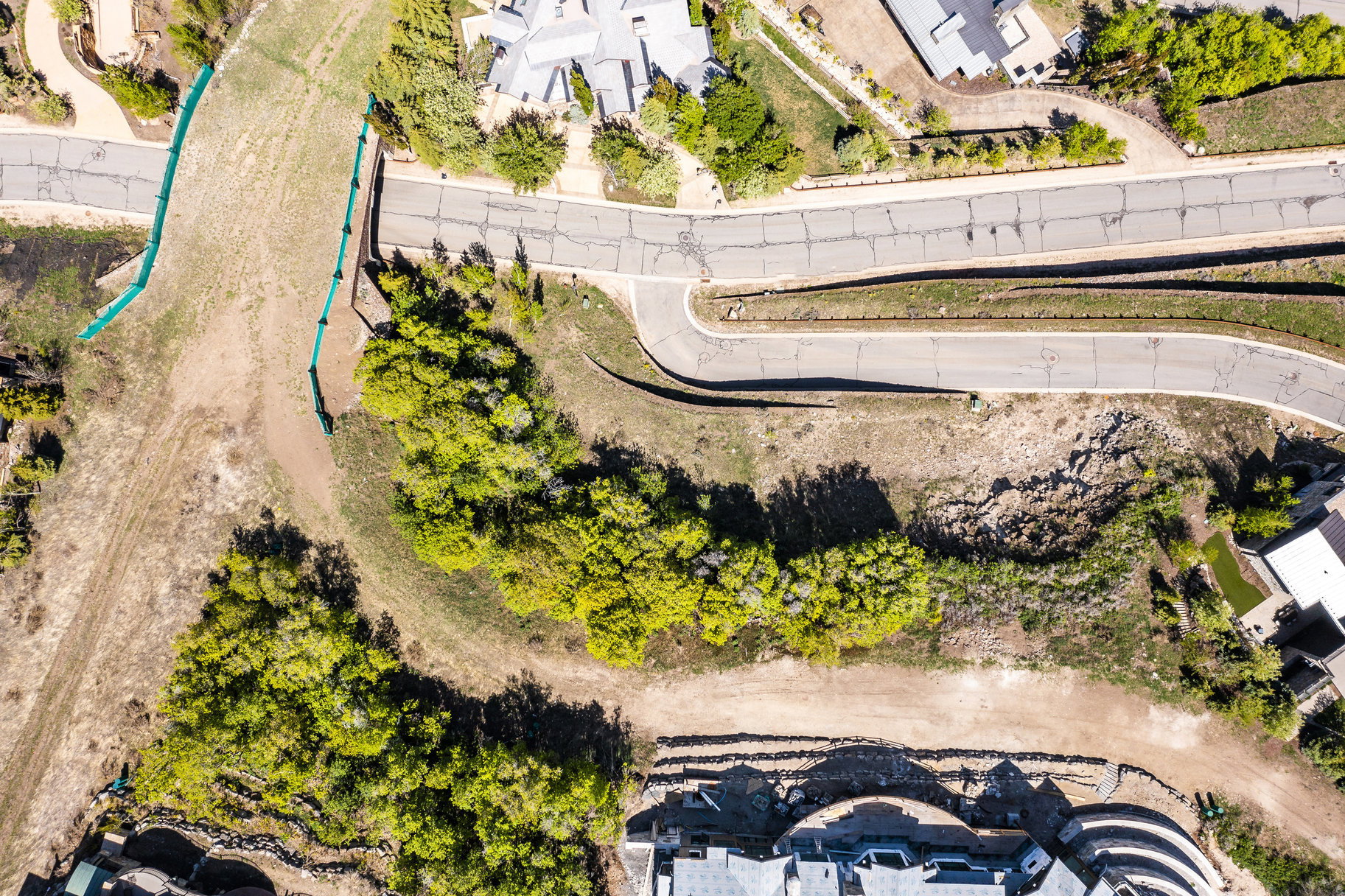 Aerial depiction of a sloped property featuring established roadways, surrounding residences, and natural landscaping