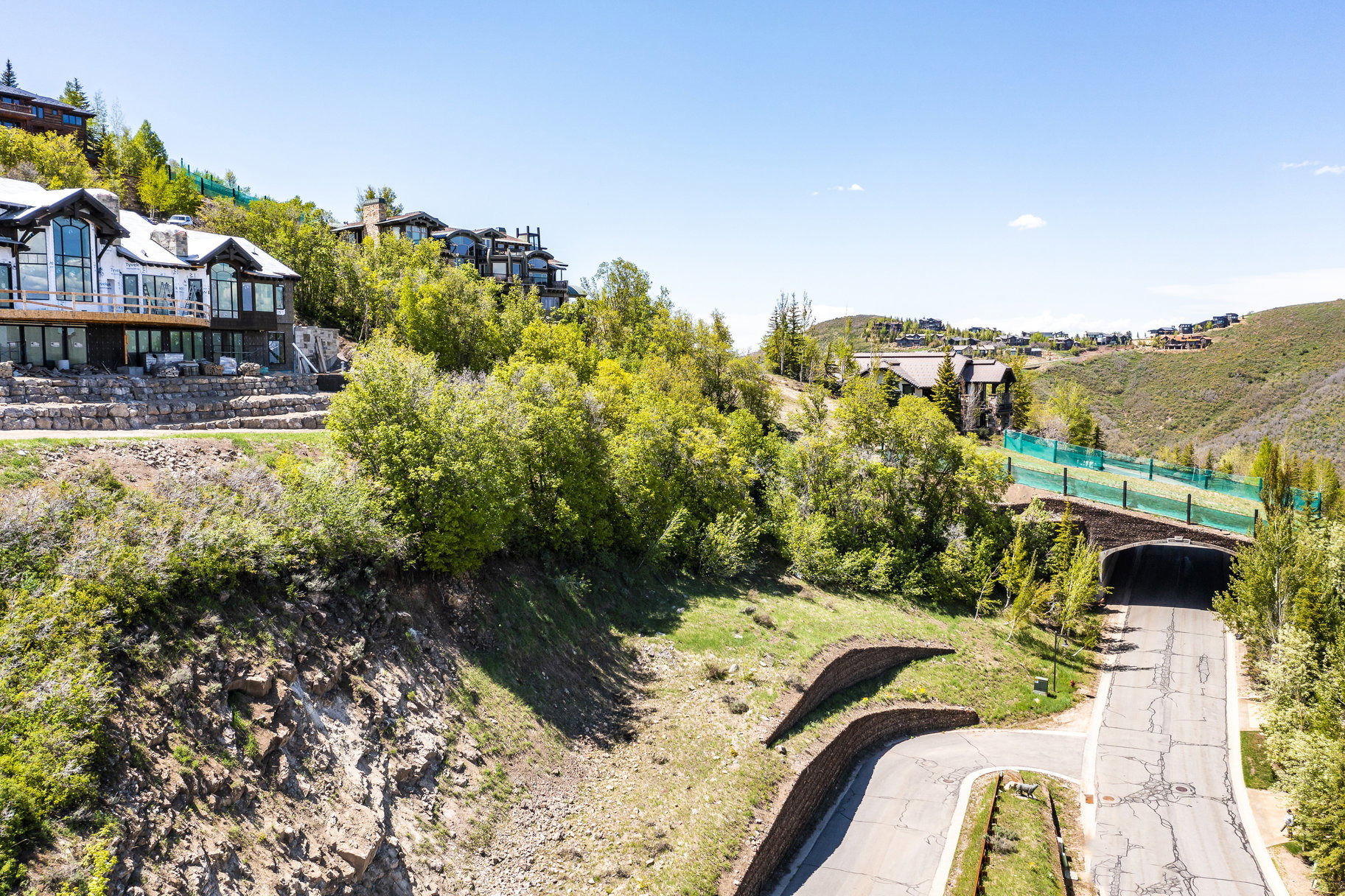 Hillside property featuring a multi-level residence with extensive glass windows, a large balcony, and stone retaining walls