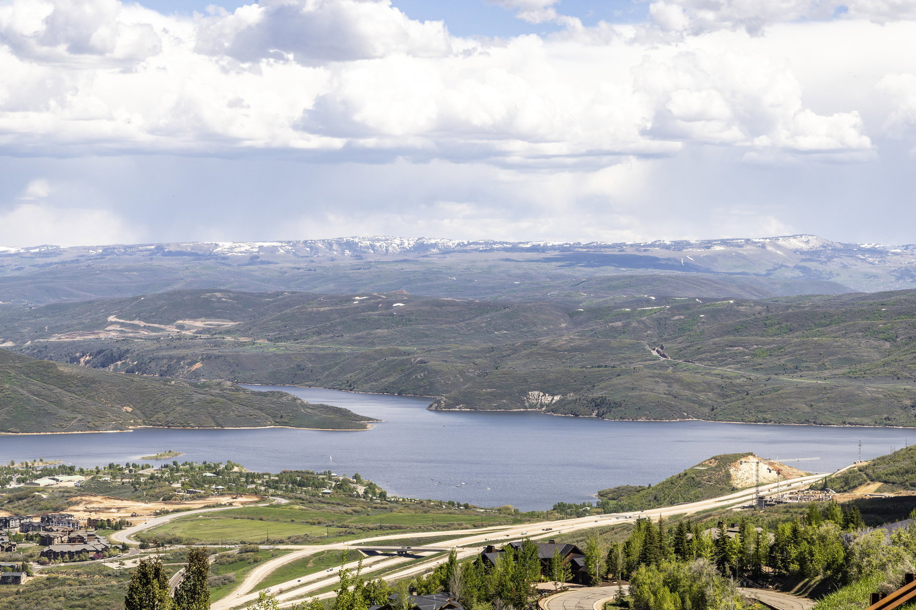 Expansive landscape featuring a large body of water, distant snow-capped mountains, and rolling green hills