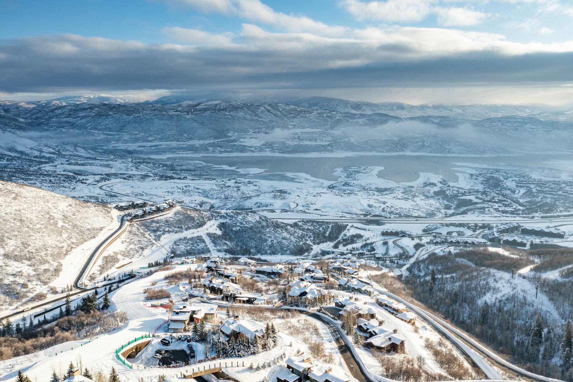 Snow-covered mountain landscape with residential properties, a body of water, and winding roads