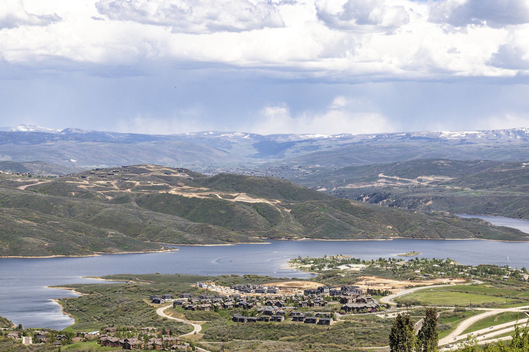 Expansive mountain landscape featuring a large body of water, distant snow-capped peaks, and scattered residential developments