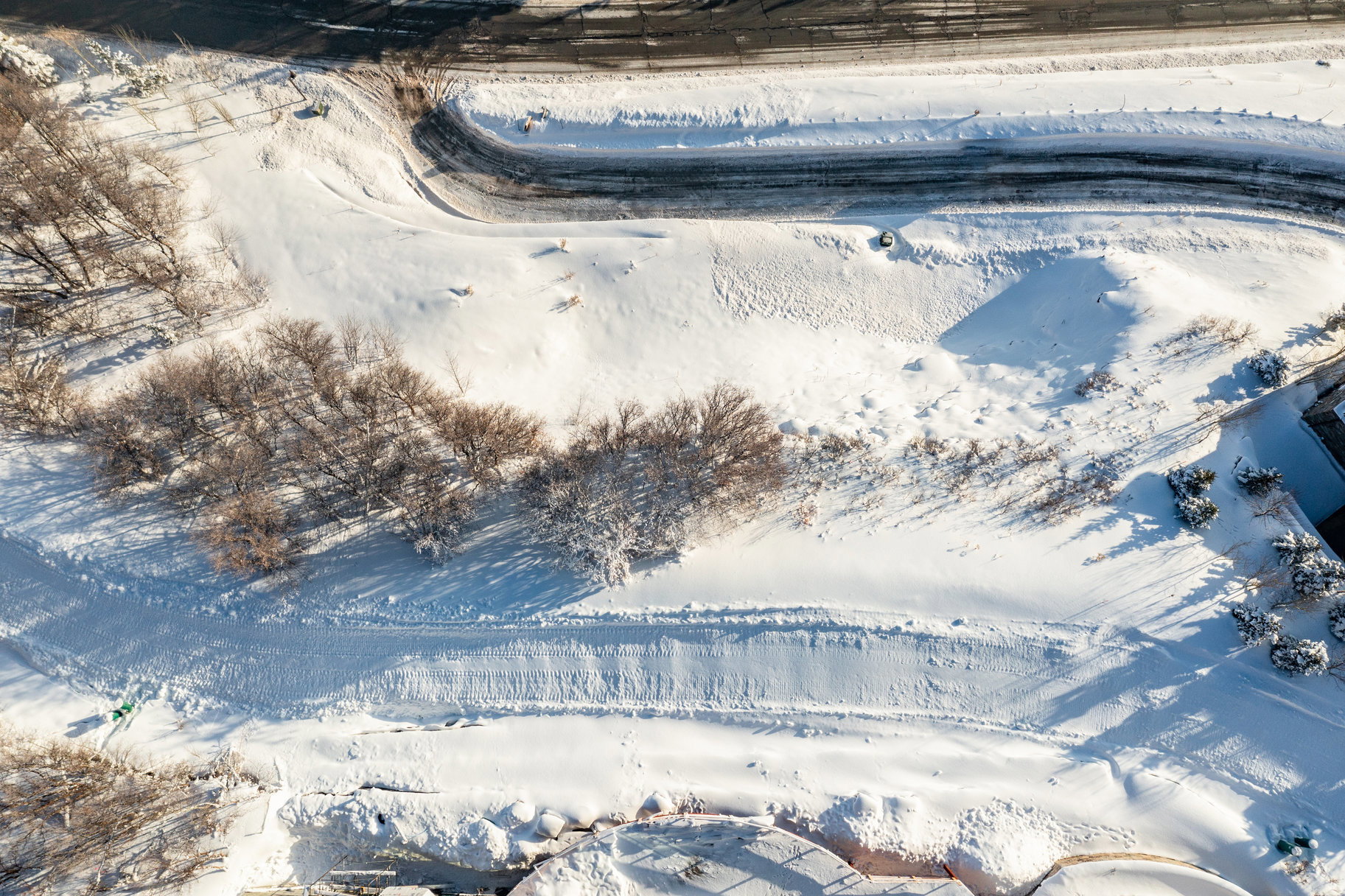 Expansive snow-covered terrain featuring a paved road, multiple trees, and a building structure
