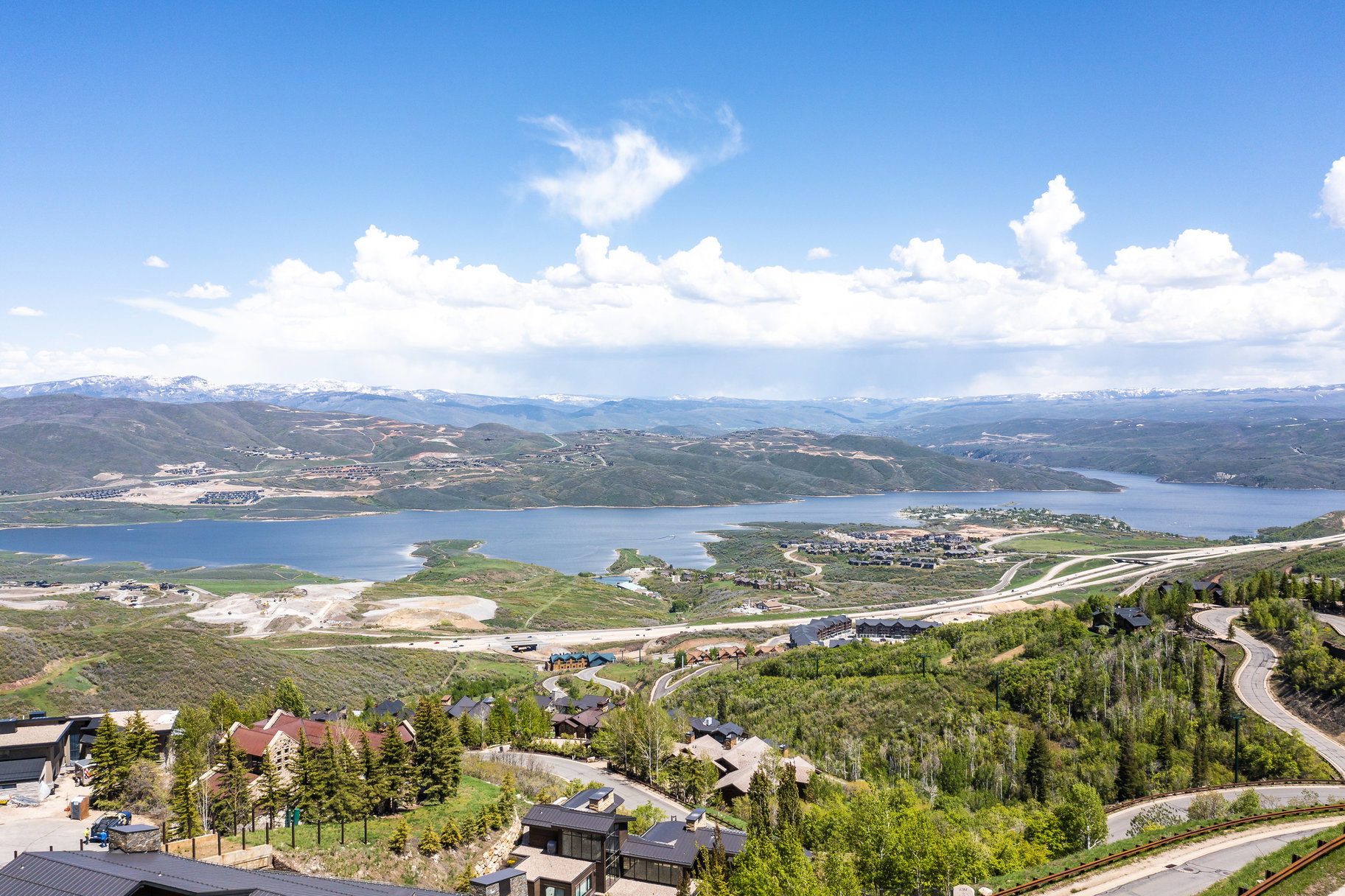 Expansive mountainous landscape featuring a large body of water, distant snow-capped peaks, and scattered residential properties