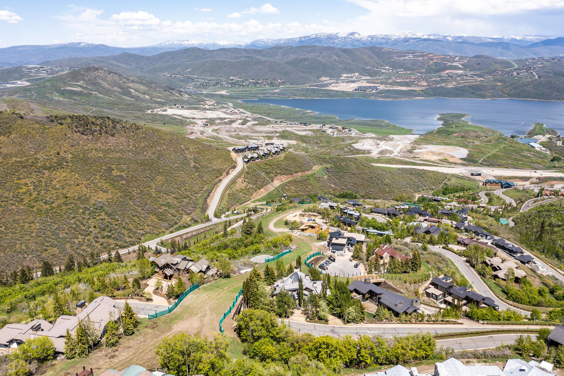Expansive mountainous landscape featuring a large body of water, distant snow-capped peaks, and a developed hillside with multiple properties