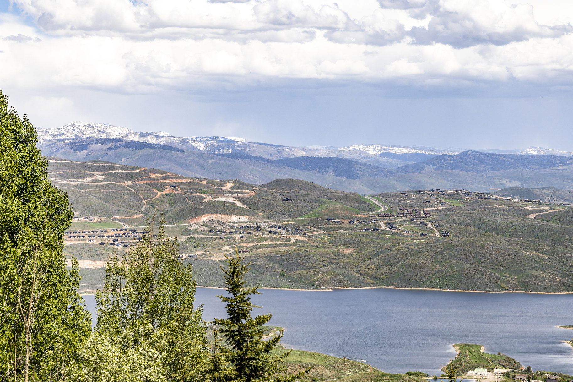 Expansive mountain landscape featuring a large body of water, distant snow-capped peaks, and scattered residential developments