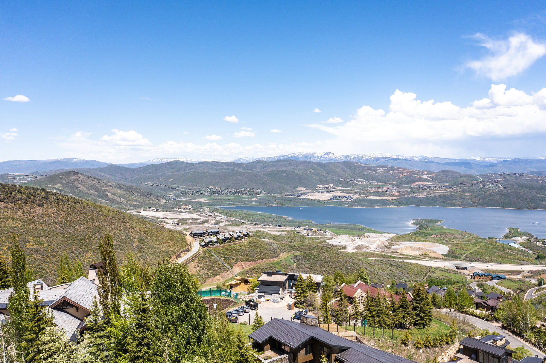 Expansive mountain landscape featuring a large body of water, distant snow-capped peaks, and scattered residential properties