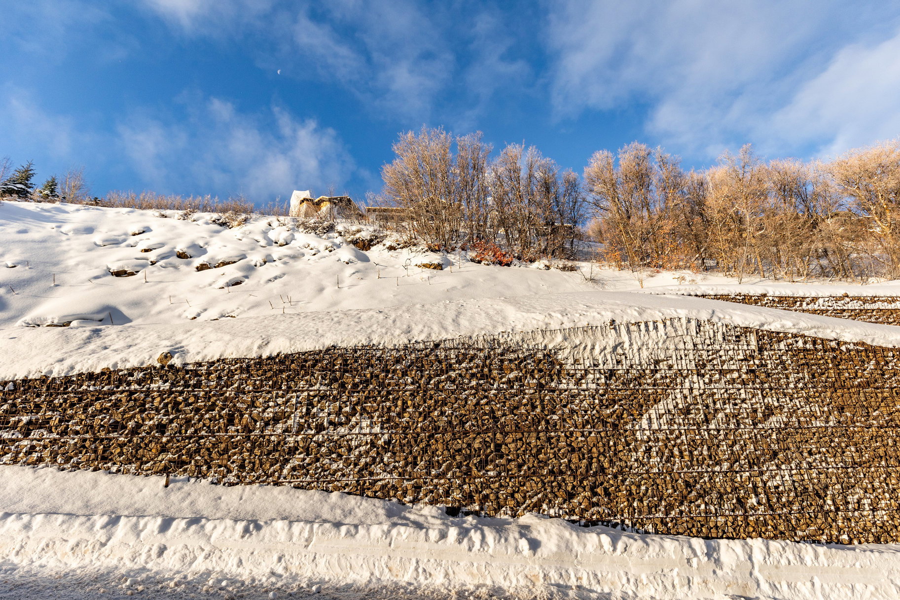 Layered gabion retaining walls provide structural support to the snow-covered hillside
