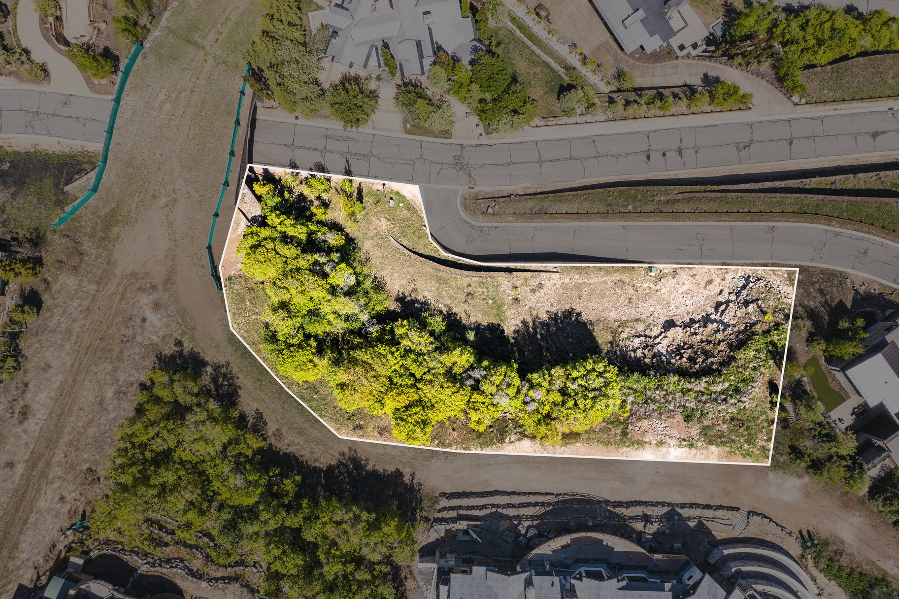 Expansive undeveloped lot featuring mature trees and varying topography, bordered by paved roadways and existing structures