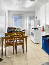 Kitchen with white appliances, a textured ceiling, white cabinetry, light tile patterned flooring, and light countertops