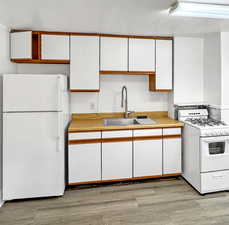 Two tone kitchen featuring white appliances, light countertops, two tone cabinets, and light wood-style floors