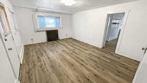 Unfurnished bedroom with light wood finished floors, radiator, and a textured ceiling