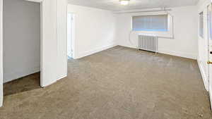 Unfurnished bedroom with light carpet, radiator, and a textured ceiling