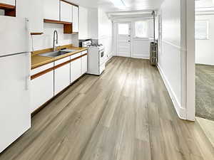 Kitchen featuring dual tone cabinets, white appliances, light wood finished floors, light countertops, and radiator