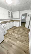 Kitchen with white cabinetry, white appliances, a textured ceiling, glass fronted cabinets, and light wood-style flooring