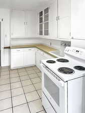 Kitchen with white range with electric stovetop, white cabinets, glass insert cabinets, light tile patterned floors, and light countertops