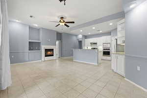 Kitchen featuring stainless steel appliances, a glass covered fireplace, built in shelves, white cabinetry, and open floor plan